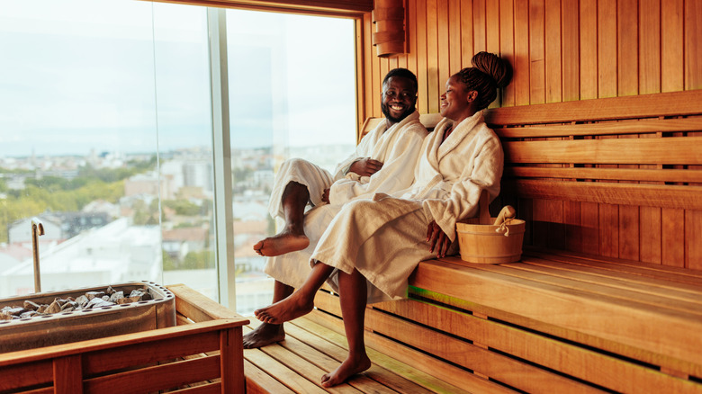 Black couple in white robes smiling and sitting in a sauna with a view