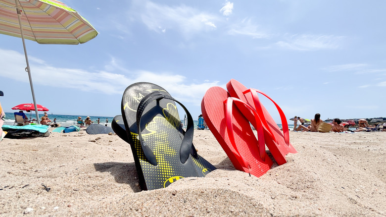 Colorful flip flops stuck in the sand at a vibrant beach, surrounded by umbrellas and sunbathers