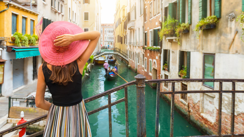 Elegant woman with red sunhat enjoys the view to a canal with passing by gondola in Venice, Italy