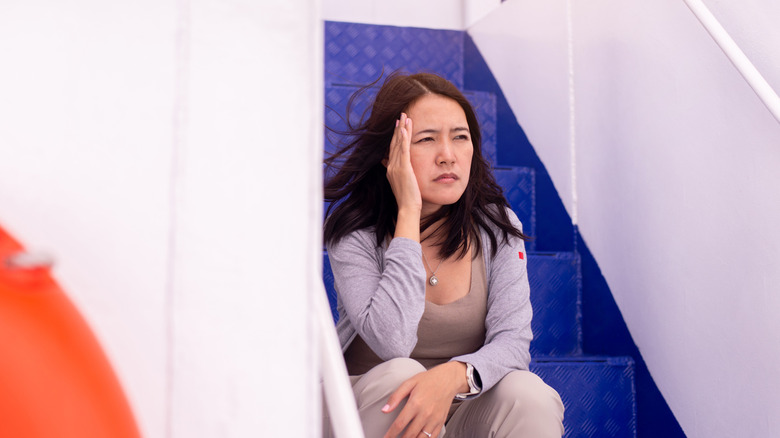 A woman sitting on the steps of a boat with a pained expression and touching her head