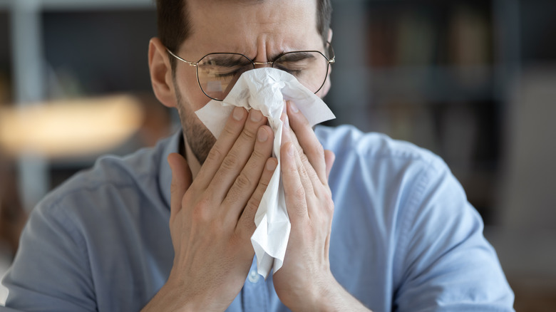 A man with the flu, blowing his nose into a tissue