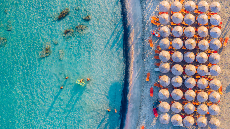 Aerial view of pink umbrellas on the pink Elafonissi Beach near clear blue water on Crete, Greece