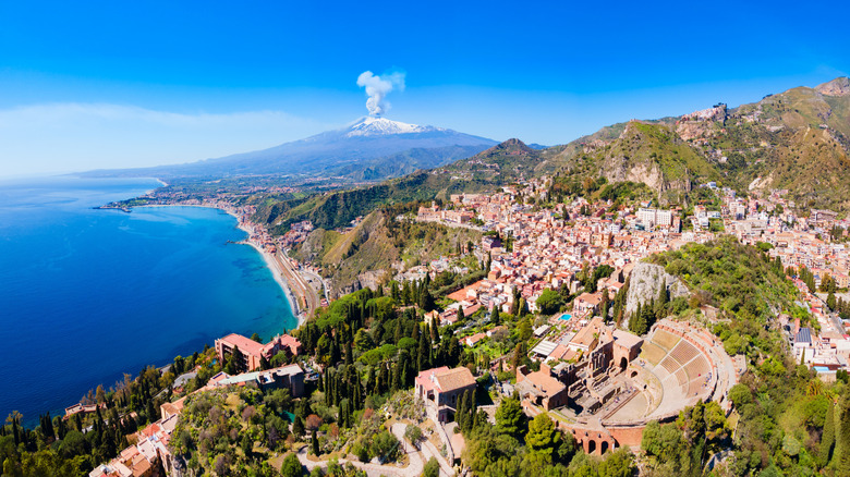 Aerial view of the coast of Sicily with Mount Etna volcano in the background emitting a puff of steam