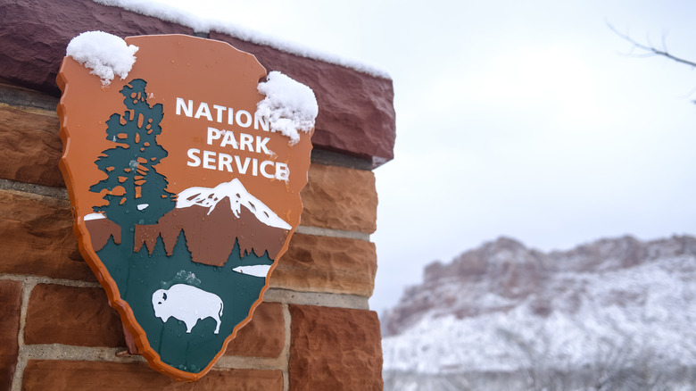 A National Park Service plaque is pictured with snow-covered terrain in the background.