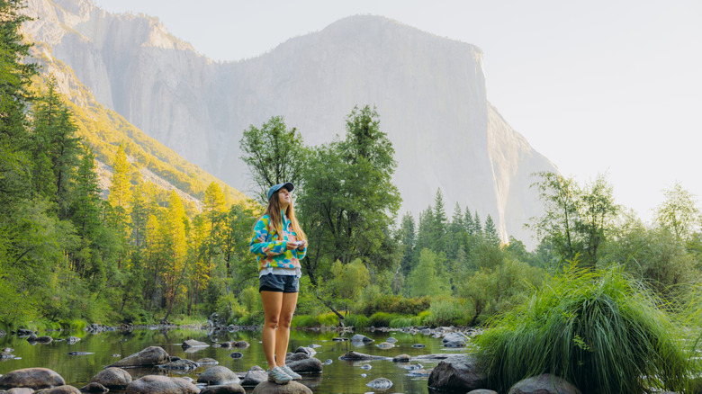 A female hiker stands on a rock in a creek in Yosemite National Park, California, United States.