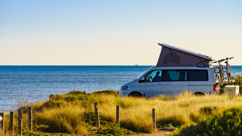 A camper van with a rooftop tent faces the open ocean.