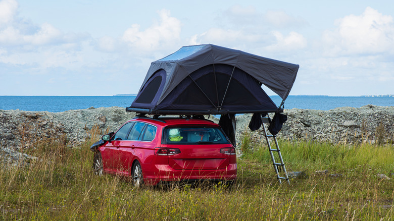 A red car with a rooftop tent parked facing the ocean.