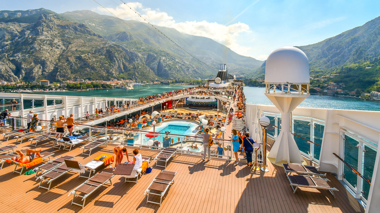 The crowded upper deck of a major cruise ship, featuring a small pool at its center.