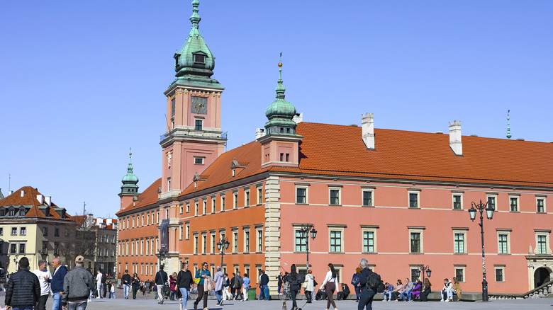 The exterior of the Royal Castle in Warsaw, with pedestrians walking and sitting outside