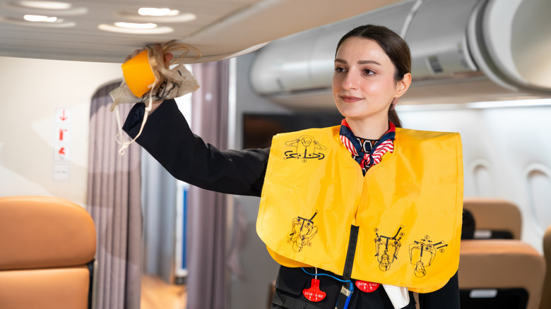 A flight attendant wearing a life vest shows how an oxygen mask will drop in the event of a decompression during the safety demonstration.