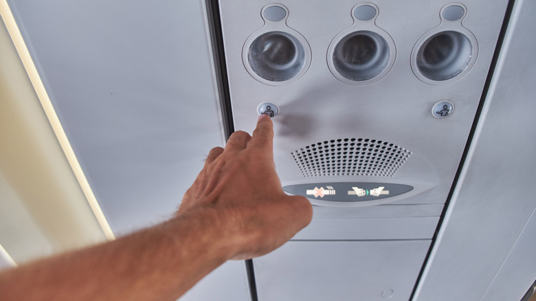 A hand reaches up to ring the flight attendant call button on an airplane.