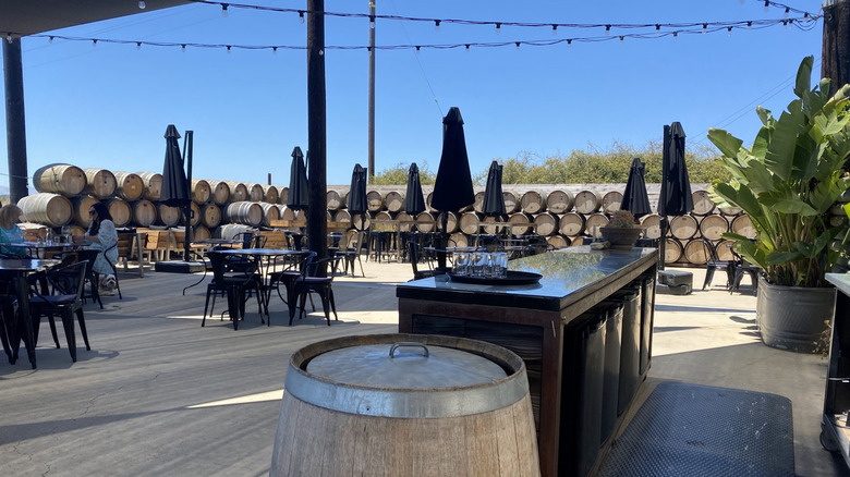 Chamisal Vineyards seating area with tables and closed umbrellas, surrounded by barrels