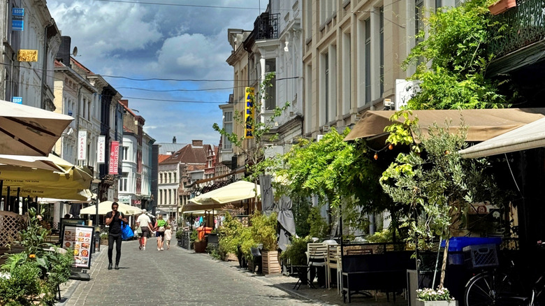 Cobblestone road in Ghent lined by historic buildings and cafe patios with umbrellas.