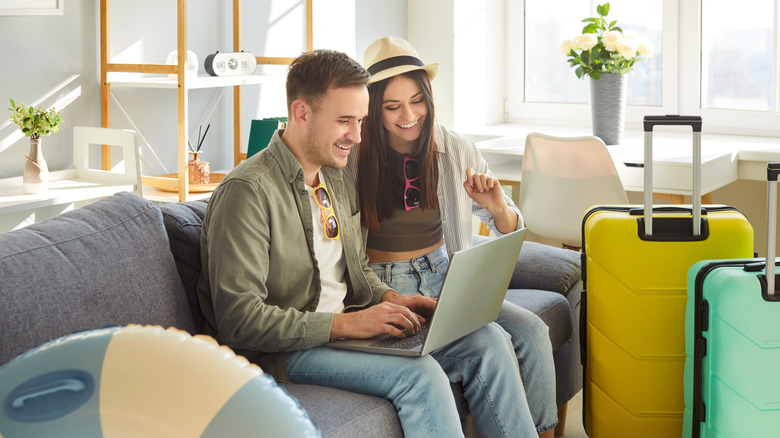 cheerful couple using laptop while close to their luggage