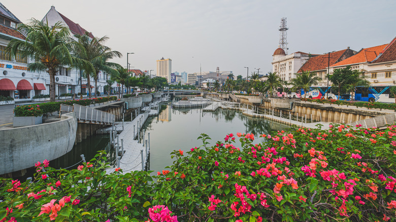 A scenic canal winds through a historic city center, lined with vibrant flowers and colorful buildings with traditional architecture.