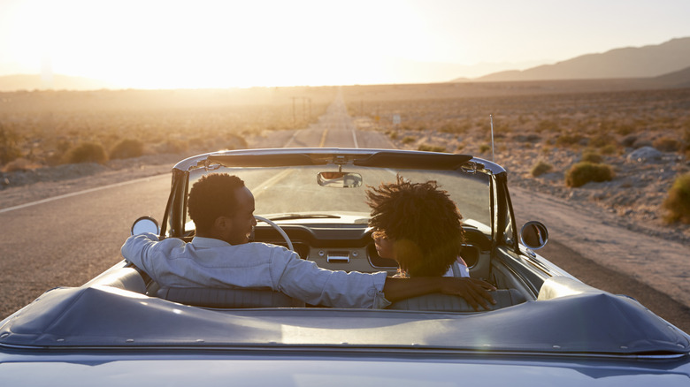 Couple with curly hair riding into the sunset in a convertible on an empty highway in the American West desert landscape
