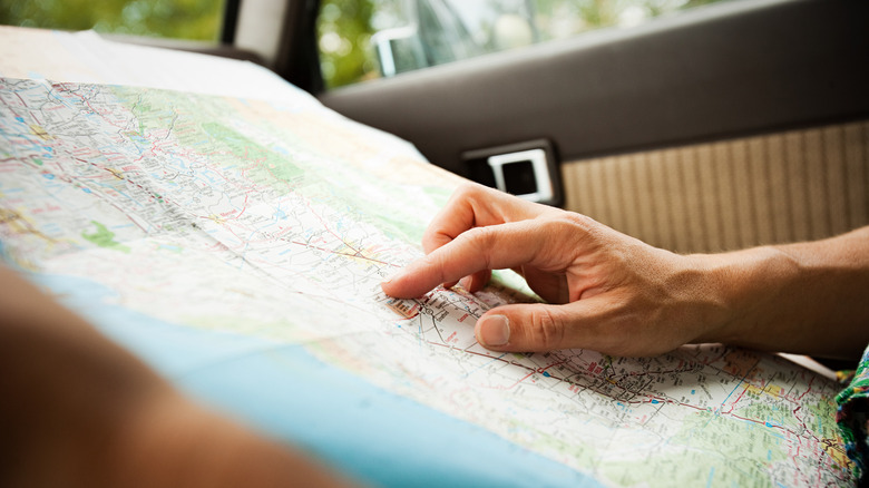 Person pointing at a paper map of the western United States while riding in a car's passenger seat