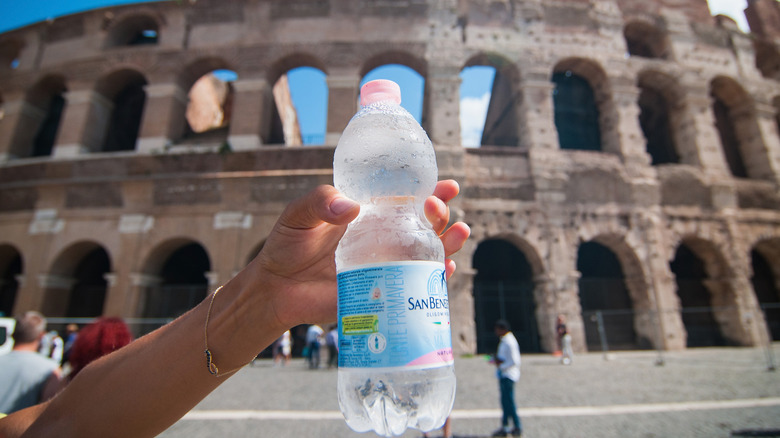 Person holding up a bottle of water in front of the Colosseum in Rome