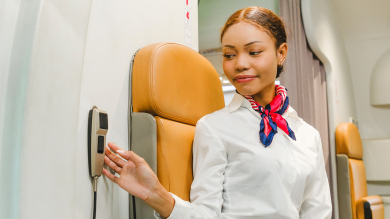 A flight attendant reaching for an intercom on the wall of a plane cabin