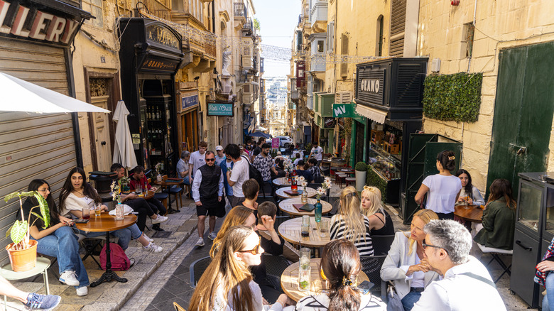 Customers sit at outdoor tables in a narrow street in Valletta