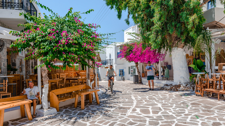 Traditional cobblestone alley with whitewashed houses, bougainvillea trees, and sidewalk cafes in Paros, Greece