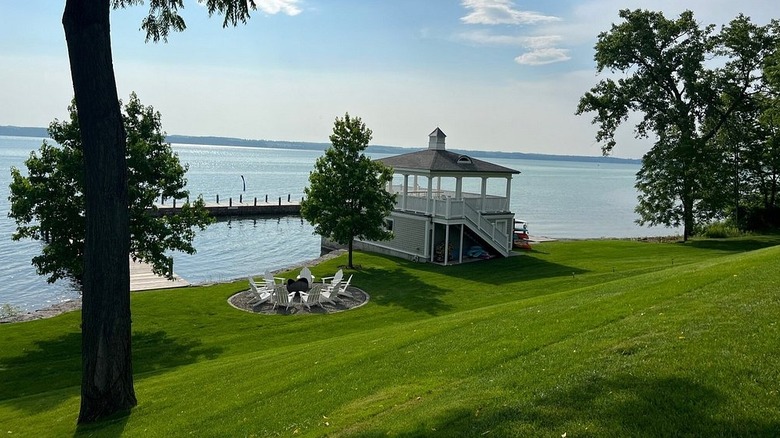 A waterfront area with a lawn, chairs around a fire pit, and a gazebo