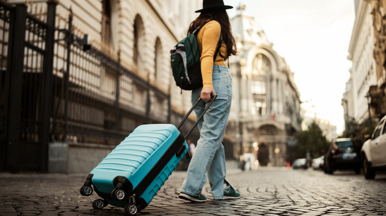 Woman in yellow pulling a blue suitcase on the cobblestone streets of Bucharest, Romania