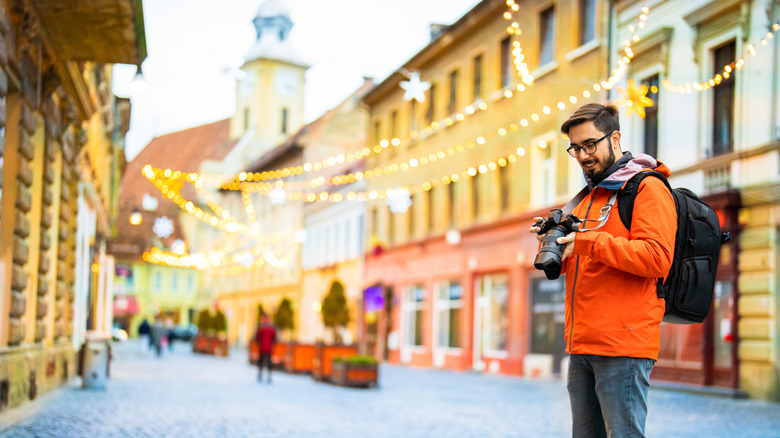 Bearded man in an orange jacket looks at his camera on the old streets of Brasov, Romania