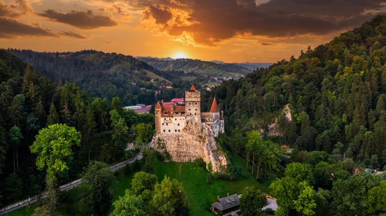 Aerial view of Bran Castle high on a rock in the Transylvanian mountains in Romania surrounded by green forest during sunset