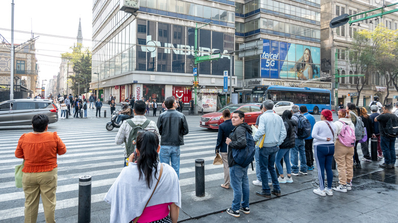 Pedestrians wait at a zebra crossing in a busy urban street scene in Mexico City