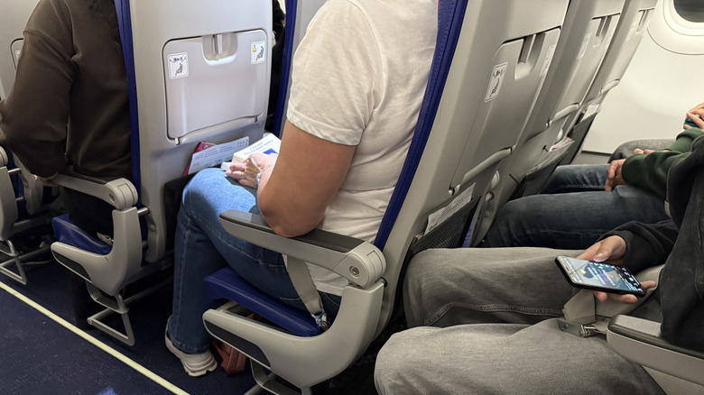 Passengers seated in rows of plane seats with narrow legroom