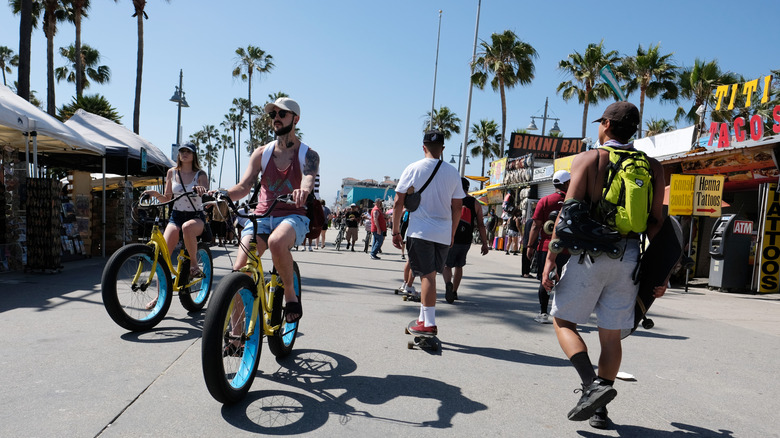 Cyclists, skaters, and pedestrians share the boardwalk amongst vendors and palm trees