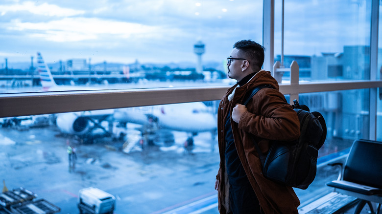 A man looking out the window at an airport on a rainy day