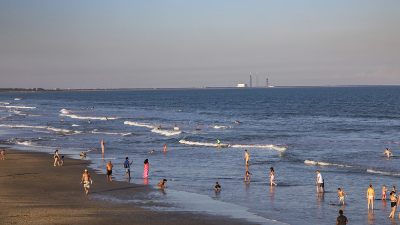 People of all ages wade and play in the shallow waters along the shoreline at Cocoa Beach, Florida.