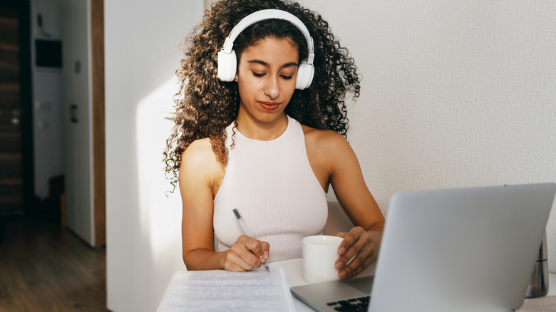 A woman wearing headphones studying with a laptop and paper