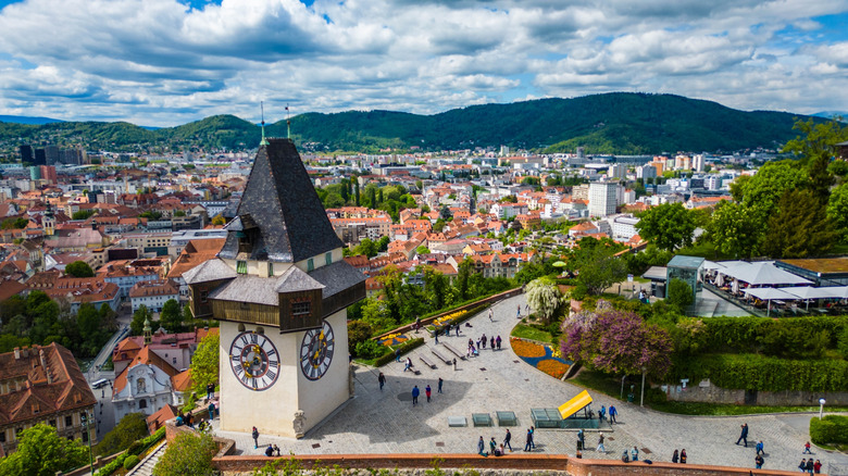 Aerial view of Graz, Austria, with a mountainside observation deck with a clock tower overlooking orange-roofed houses