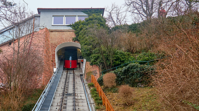 Schlossberg's red funicular in Graz, Austria, ascending steep track through tunnel entrance surrounded by greenery