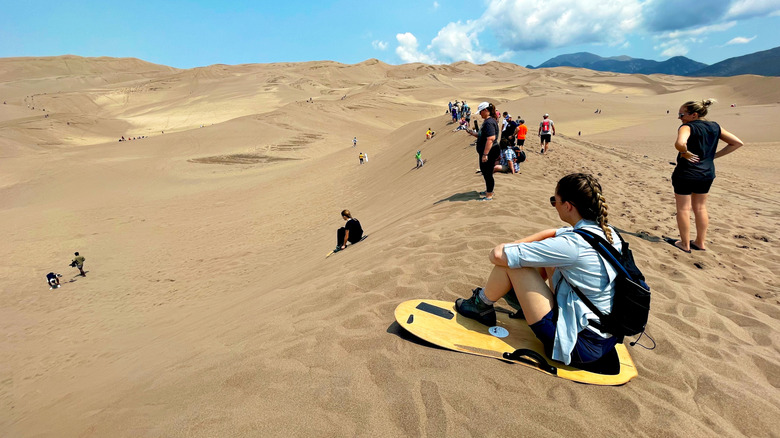 woman sitting on a sandboard with fellow tourists watching at Great Sand Dunes National Park