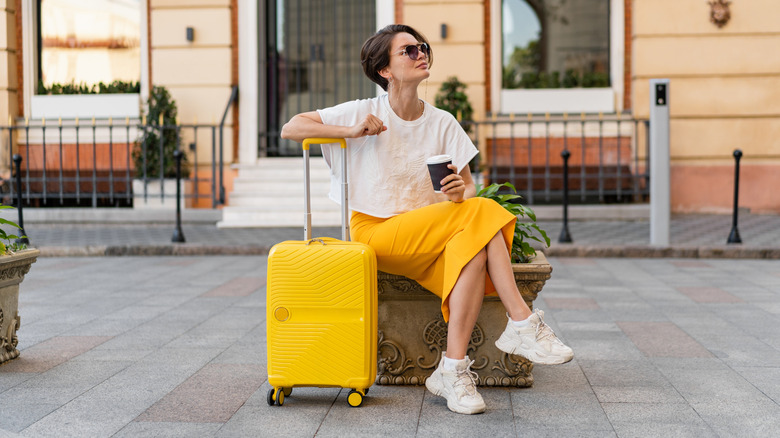 Woman sitting outside with her arm leaning on a yellow suitcase