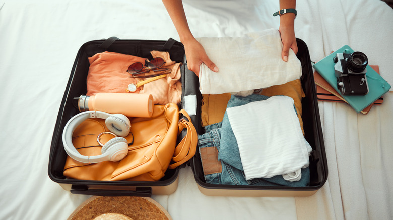 Someone packing a suitcase on a bed