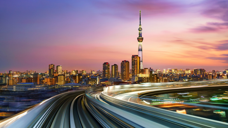Long exposure photo of the Tokyo Skytree towering over the city skyline with a blurred highway in the foreground and a dusky pink sky in the background