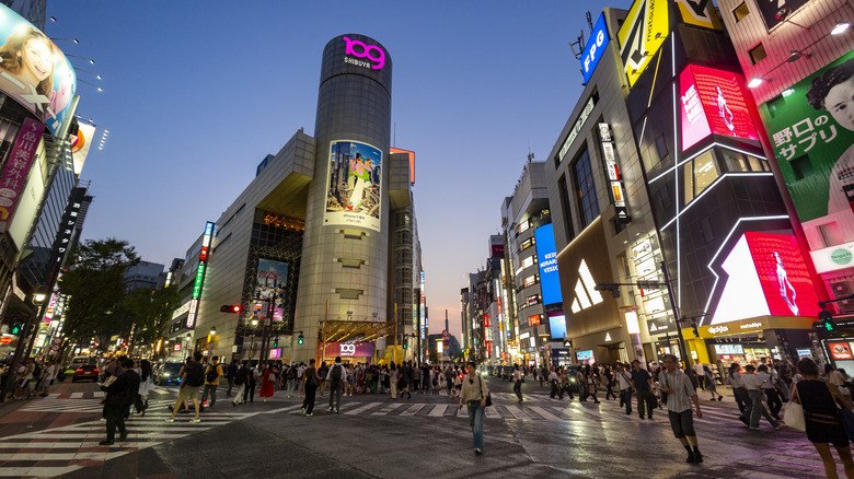 View of Shibuya Crossing at dusk surrounded by neon lights.