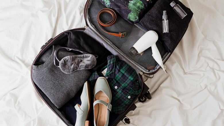 An open suitcase on a bed filled with clothing, shoes, and other personal items