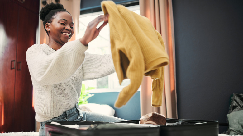 A woman sitting on a rug pulling a yellow sweater out of a suitcase