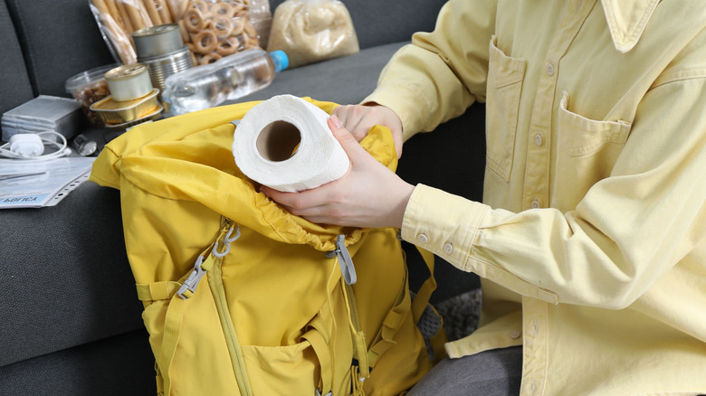 A woman placing toilet paper into a backpack