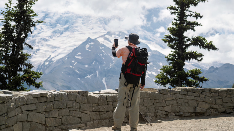 Backpacker taking photos of Glacier using a smartphone at Glacier Overlook in Mount Rainier National Park.