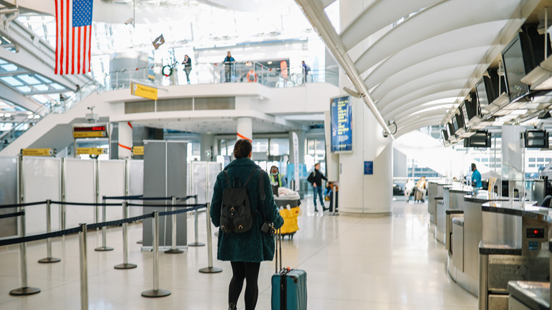 A woman with a rolling suitcase walks past an empty airport security line in the U.S.