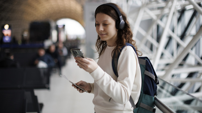 A teenage girl with headphones using mobile phone at the airport.