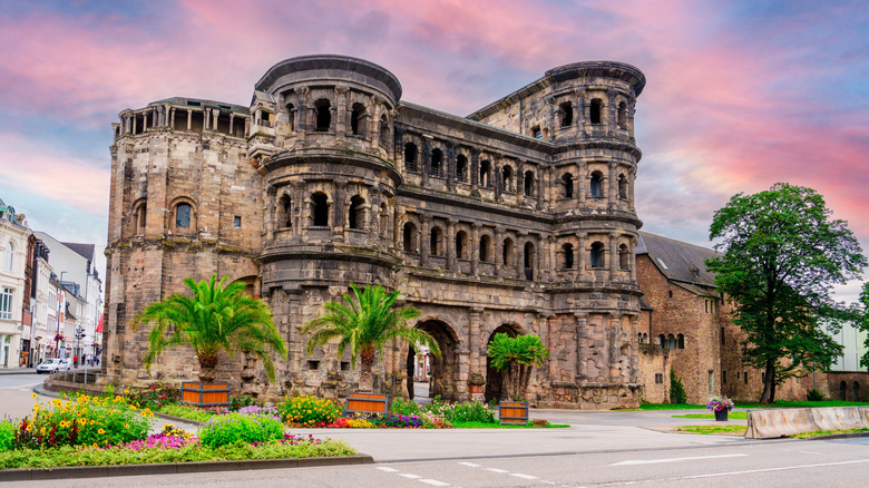 Trier's famous Roman gate, Porta Nigra, blackened with age, surrounded by greenery, under a pink sky