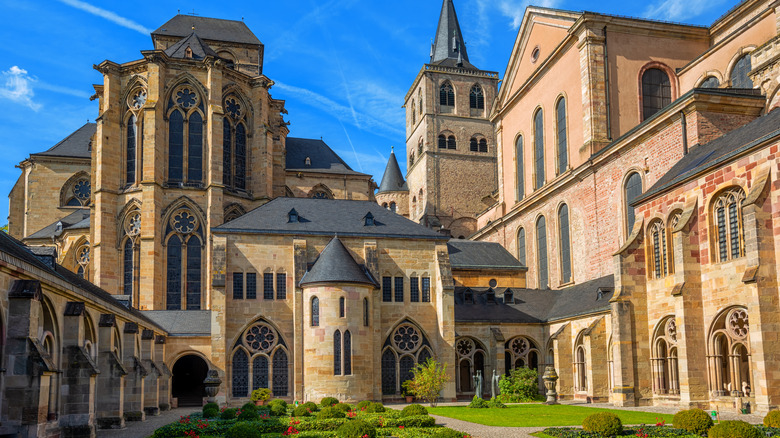 Trier Cathedral built out of stone with ornate windows and arches stands tall over a green courtyard, Germany